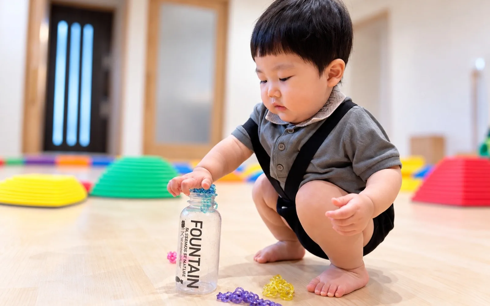 しゃがんでボトルにビーズを集中して入れるお子さま